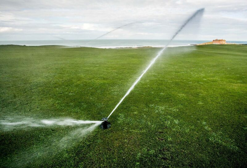 A close up of a Toro Irrigation sprinkler operating over a golf course.