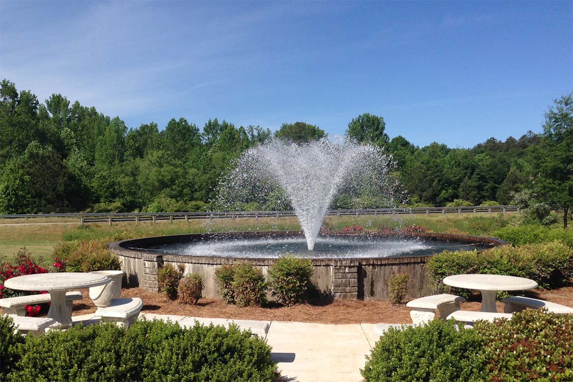 An Otterbine aerating fixed fountain in the middle of a small oval pond.